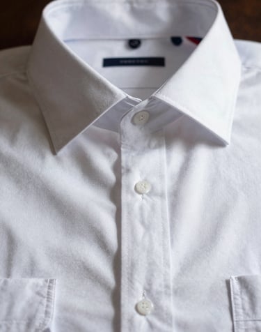 Close-up of a crisp white premium cotton dress shirt, perfectly ironed collar, soft dramatic shadow casting over the structured placket.