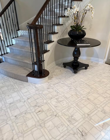 Elegant foyer featuring marble tile flooring, a carpeted staircase with wood banister, and a round accent table.