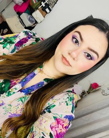 Mujer con cabello largo y oscuro que usa sombra de ojos violeta y una blusa con estampado floral 