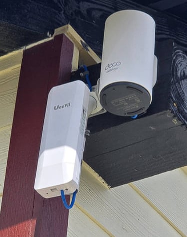 TP-Link Deco outdoor mesh WiFi node and UeeVii wireless bridge mounted on a house exterior.