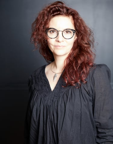 Marion Herlédan is a woman with red hair and glasses on a black background she is a food photographe