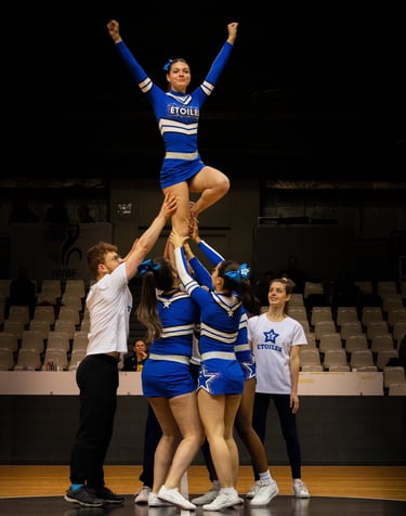 A cheerleading flyer in a blue uniform performs a stunt being lifted by her team during a competition.