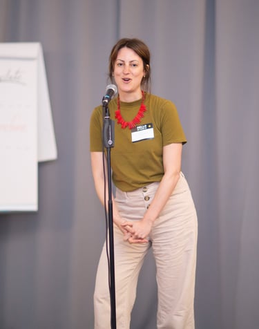 Young woman speaking behind microphone, flipchart in the back showing teachings of seminar