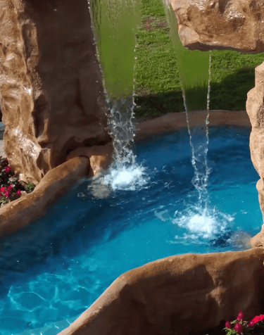 Backyard rock waterfall feature with cascading water flowing into a bright blue swimming pool.