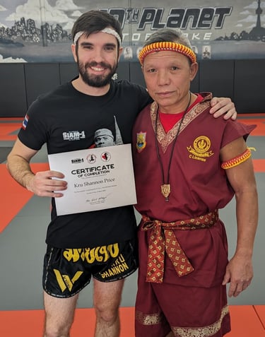 Kru Shannon stands next to Ajhan Suchart after recieving his Kru Certification.