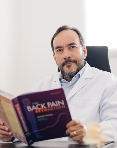 Neurocirurgião Dr. Carlos Moreira especialista em coluna lendo livro sobre dor em consultório.