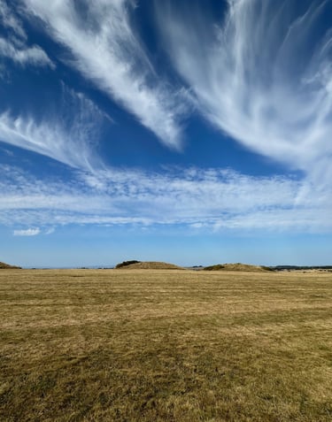 Dramatic clouds sweep up over a deep blue sky above a hilltop in the Mendips, with burial mounds
