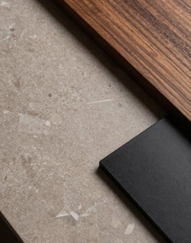 A top-down view of design materials on a workspace: a slab of taupe marble, a piece of dark wood, and a matte black hardware sample, representing premium craftsmanship.