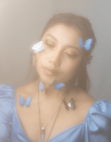 A dreamy and hazy self portrait of a young adult Asian woman, blue butterflies on face and neck