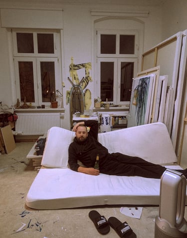 Artist relaxing on a floor mattress in his messy creative studio with paintings