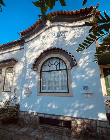 Traditional white Portuguese villa with arched windows, red tile roof, and green door in sunlight.