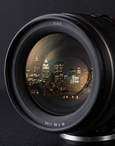 A close-up, artistic shot of a high-end cinema lens reflecting a North American / US skyline at night. The image exudes a premium feel with deep black, charcoal grey, and subtle muted gold light flares.