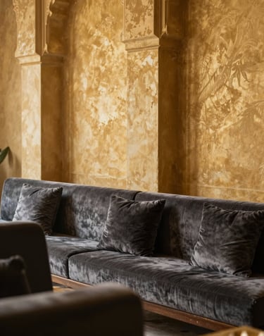 An elegant interior detail of a luxury lounge in a North African / Moroccan palace. Muted Gold textures on the walls and Charcoal velvet seating, lit by soft natural light.