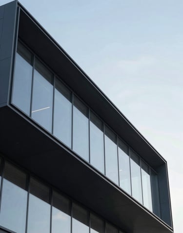 Detail of modern architectural facade with clean lines, large glass panels, and very dark charcoal metal accents against a clear sky.