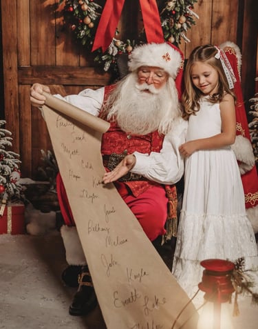 Santa Claus reading his long list of names to a little girl in a white dress by a Christmas tree.