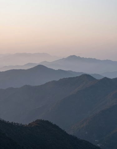 A wide landscape shot of a misty mountain range at dawn, emphasizing quiet confidence and the scale of travel possibilities, utilizing #4A7B8E tones.
