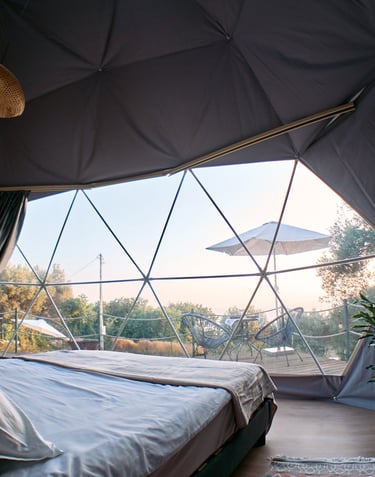 Unutrašnjost glamping kupole sa pogledom na more i udobnim krevetom