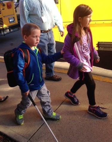 Two children using canes while getting off a school bus, showcasing independent mobility for student