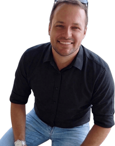 A smiling man wearing a black button-down shirt, blue jeans, and sunglasses on his head.