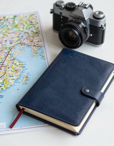 A flat lay of travel essentials: a physical map, a classic camera, and a leather-bound journal. The composition is elegant and organized, featuring colors like #1C2C39 and #3E6B7A.