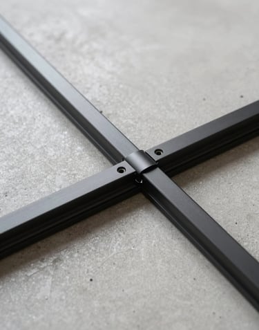 Detailed close-up of a minimalist sliding door track recessed perfectly into a light gray concrete floor. The focus is on the precision alignment and the sleek matte black finish of the ultra-thin aluminum rail.