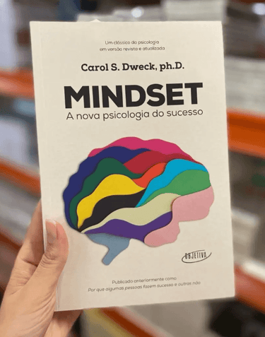 Hand holding the book Mindset by Carol S. Dweck in Portuguese, featuring a colorful brain illustration.