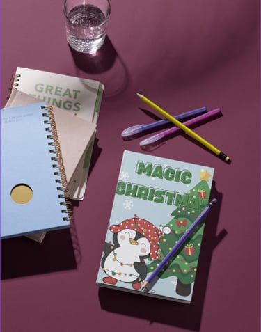 Magic Christmas penguin coloring book on a purple desk with stationery and a water glass.