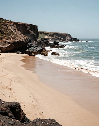 A panoramic view of the Atlantic coast near Agadir, featuring soft sand beaches and a deep espresso rocky cliffside under a bright sky.