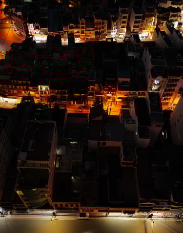 a city street scene by night with warm lights & with cars parked on the street - by ACAT PHOTOS