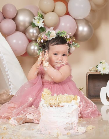 a baby girl in a pink dress and a cake