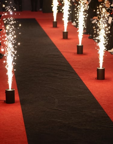 A high-angle photograph of a red carpet event in Seoul, South Korea. Golden flashes from cameras illuminate the polished black surface of the walkway, creating a sense of luxury and status.