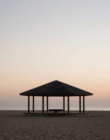 A wide-angle minimalist shot of a modern pavilion at dusk. The building is a silhouette against a soft sand colored horizon (#F9F7F2). The mood is profound and contemplative, emphasizing the architectural volume.