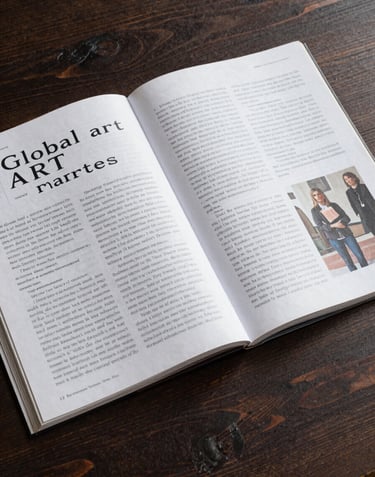 A high-angle photograph of an open art magazine with high-quality printing, showing an article about global art markets, placed on a dark wood table.