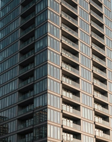 A vertical architectural shot of a modern glass high-rise facade against a clear sky. The focus is on the repetitive patterns of the balconies and windows. The style is professional and trustworthy, utilizing slate gray and off-white colors.