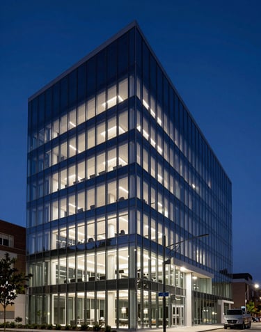 High-end commercial photography of a North American tech headquarters at twilight, showcasing clean modern lines, large glass facades, and soft pale lavender interior glows against a deep navy blue evening sky.
