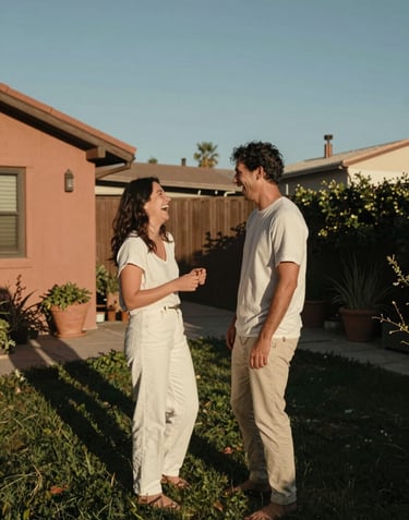 A candid, cinematic wide-angle shot of a couple laughing together in a sun-drenched North American / US backyard garden. The light is a warm terracotta glow. Colors: off-white clothing, charcoal shadows, sky blue accents.
