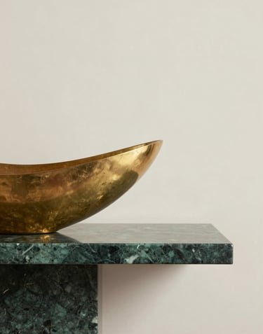 A minimalist architectural detail showing a metallic gold sculpture placed on a royal dark green marble shelf against a cream background.