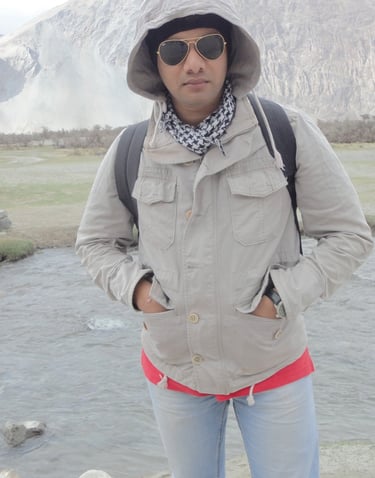 a man in a hat and sunglasses standing in front of a mountain, raheel ahmed