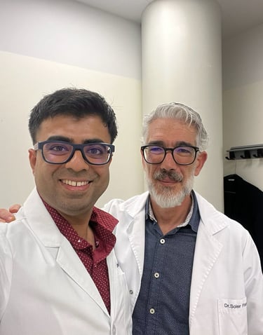 Two smiling male medical doctors in white lab coats posing for a photo in a clinical office.