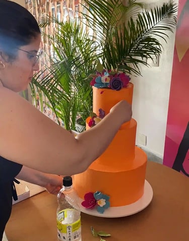Mulher trabalhando em um bolo de aniversário laranja decorado com flores em um ambiente festivo. A c