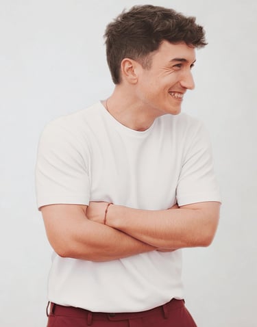 Smiling young man in a classic white crew neck t-shirt and red trousers posing with arms crossed.