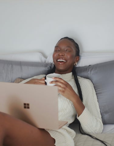 a woman sitting on a couch with a laptop and a cup of coffee with a smile on her face
