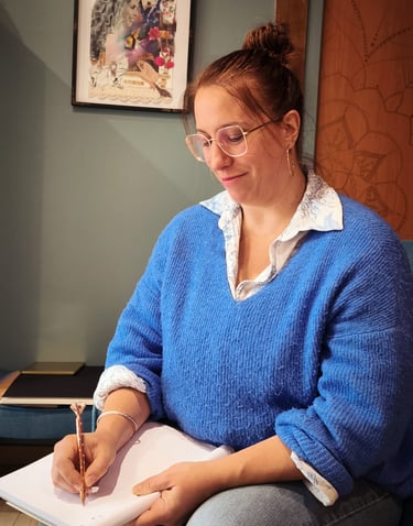 a woman in a blue sweater and glasses is writing on a notebook