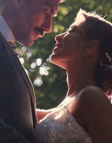 A romantic bride and groom embrace during a sunlit outdoor wedding ceremony with natural bokeh.