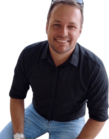 A smiling man wearing a black button-down shirt, blue jeans, and sunglasses on his head.