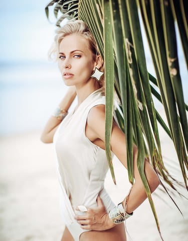 Close-up of a woman in a white bodysuit, large star earrings against a palm leaf background.