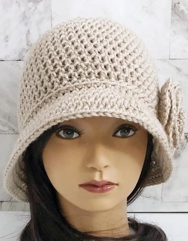 Woman wearing a tan crochet cloche hat with a large brim and flower on the side.