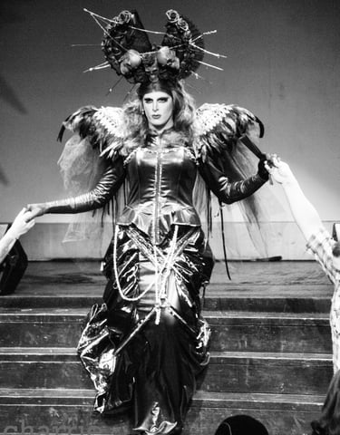 drag queen in oversized spiky hair fixture descends stage steps into audience in long gown