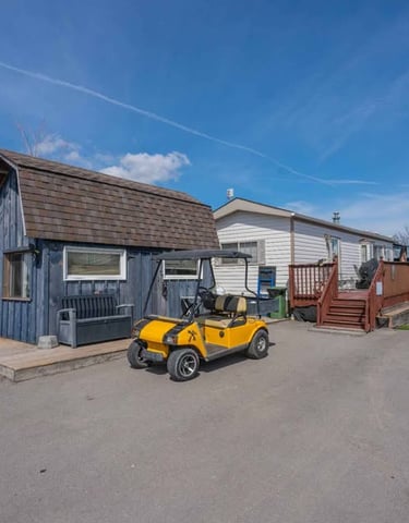 Yellow golf cart parked in front of a blue wooden shed and mobile home with a deck.