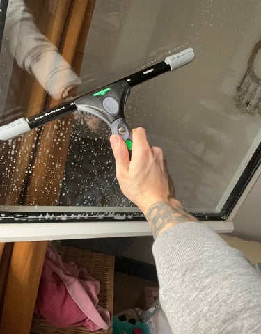 Main nettoyant une vitre avec une raclette